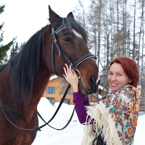 Portrait of red hair young woman at shawl with horse in winter
