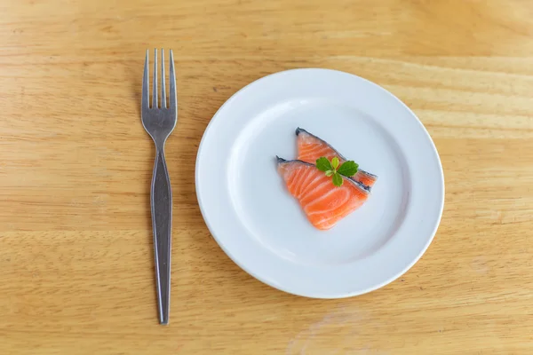 Salmon in white dish and fork on wooden