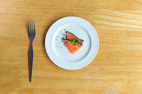 Salmon in white dish and fork on table