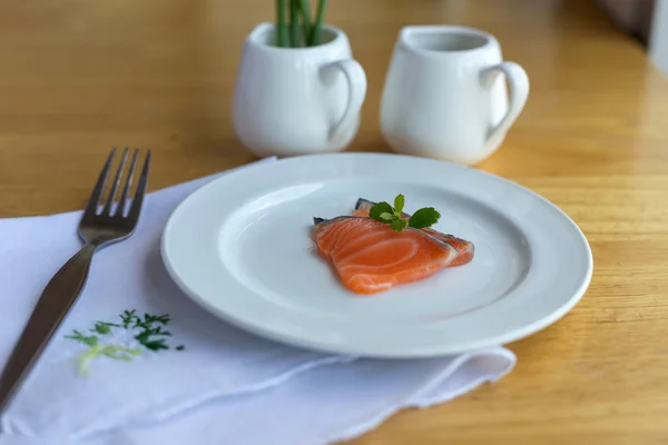 Salmon in white dish and fork on table