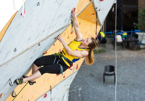 Cute female Athlete hanging on climbing Wall