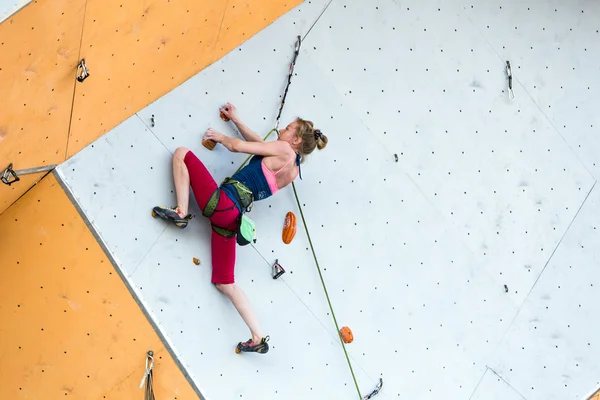 Cute female Athlete hanging on climbing Wall