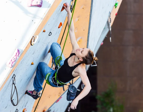 Cute female Athlete hanging on climbing Wall
