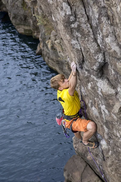 Young male rock climber hanging over the water and looking up