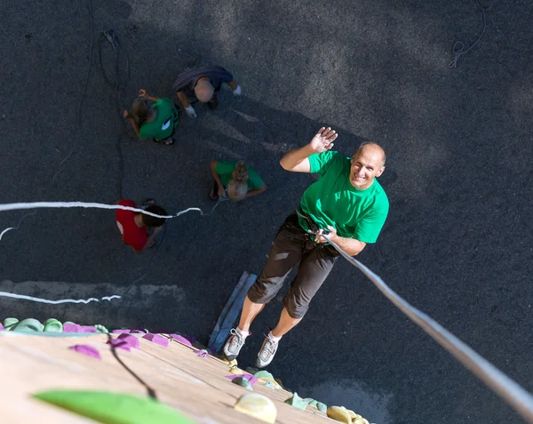 Smiling Man Descending on Rope from Top of Climbing Wall