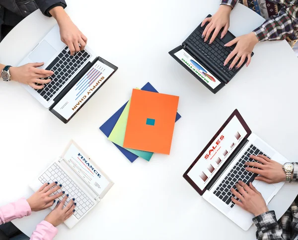 Top View of White Rounded Desk with Four Laptops and People Hands Typing on Keyboard