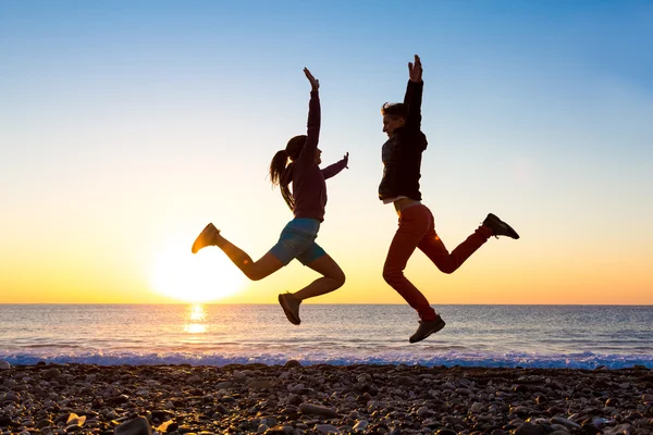 Girl and Guy jumping high with arms up spectacular sunrise at ocean coast