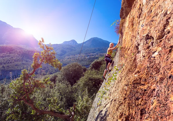 Cute blond Girl climbing orange Rock Mountains shining Sun