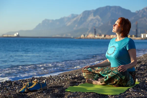 Meditating Woman on rocky Ocean Beach Mountain View on Background