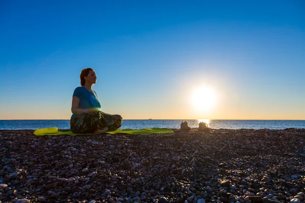 Meditating Woman on rocky Ocean Beach Sunrise background
