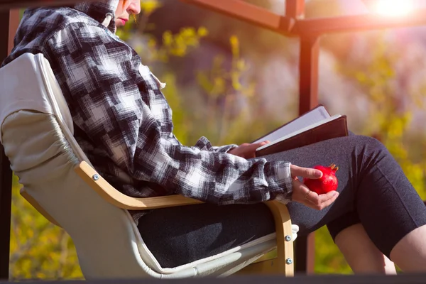 Person sitting in Chair inside rural Garden reading Book holding Pomegranate