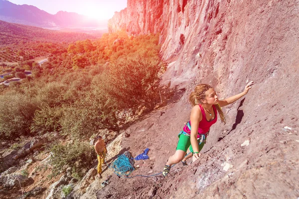 Young beautiful Female Rock Climber ascending rocky Wall