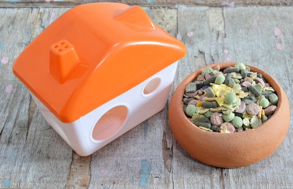 Hamster food in pottery and plastic home on wooden board