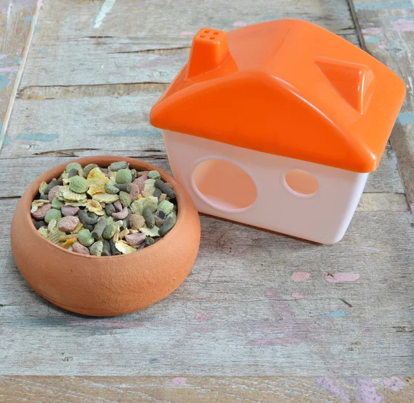 Hamster food in pottery and tiny home on wooden board