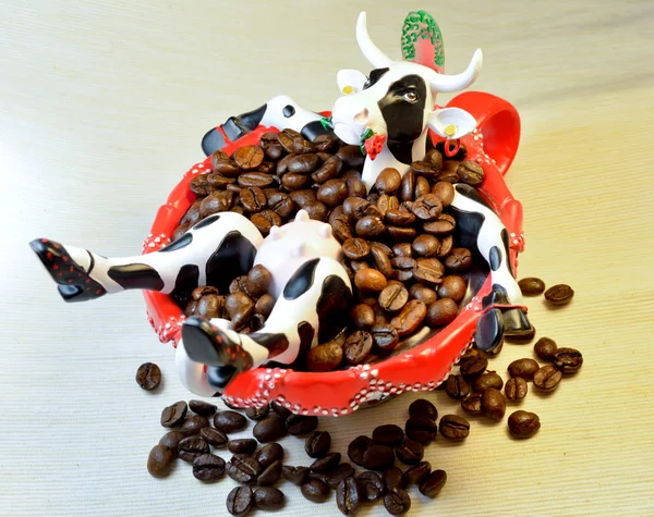 Coffee with milk: toy cow sitting in the red cup with coffee beans like in bath