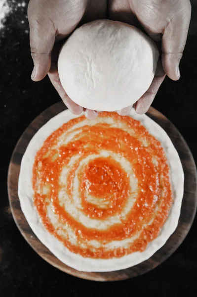 Balls of fresh pizza dough in hand and tomato sauce on pizza base