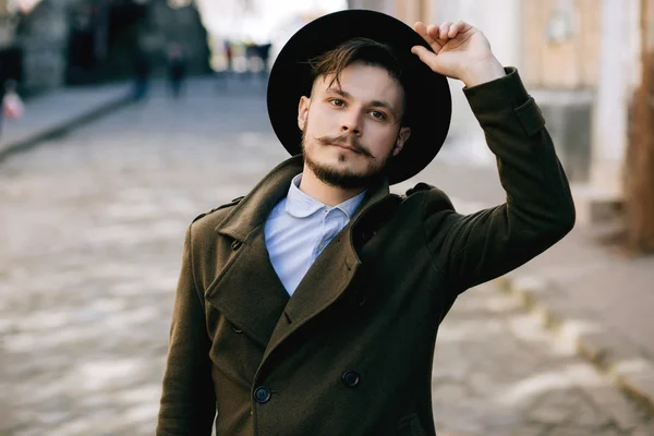 Handsome young bearded hipster man guy in hat Fedora on street with suitcase. Retro vintage fashion look