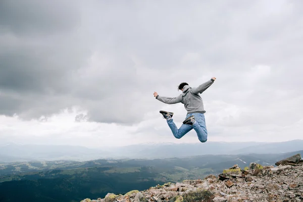 Young man Jumping Outdoors on rock in mountains sky clouds. Finish