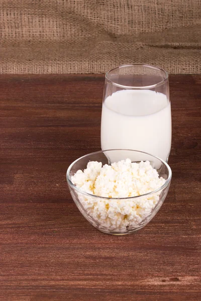 Glass cup with milk, a glass bowl with cottage cheese on a woode