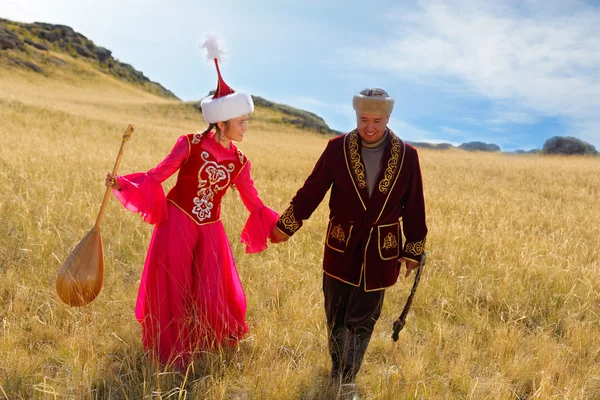 Kazakh man and woman in national costumes in the steppe playing dombyra and dancing