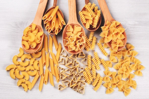 Different types of pasta lying in wooden spoons