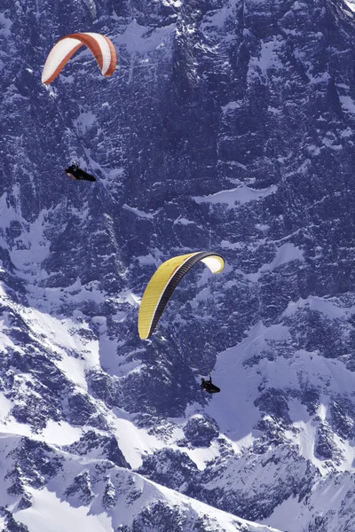 Two people paragliding in snow alps.