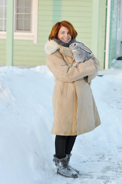 Girl with red hair in a sheepskin coat with rabbit on your hands