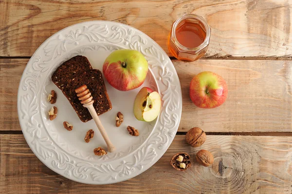 Spoon for honey with bread, apples, walnuts on a plate on wooden