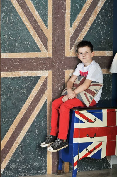 The boy sits on the nightstand on the English flag background