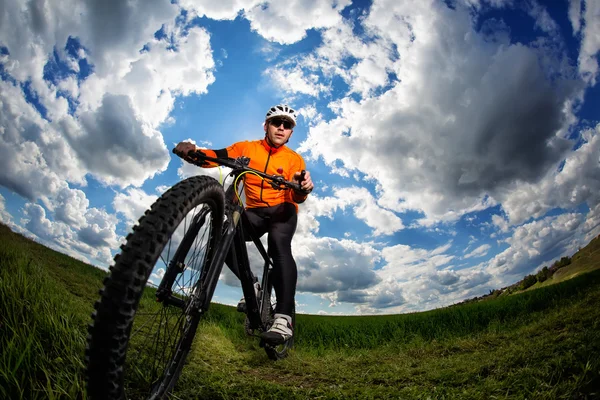 Young man cycling on a rural road through green meadow