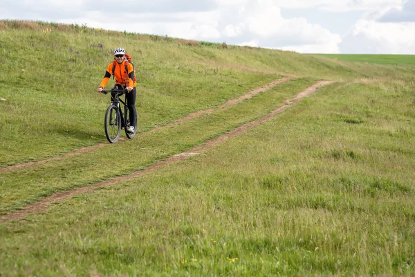 Young man cycling on a rural road through green meadow