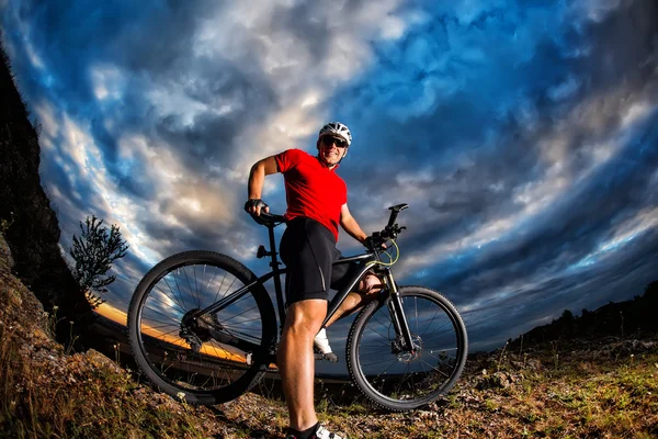 Cyclist standing with mountain bike on trail at sunset