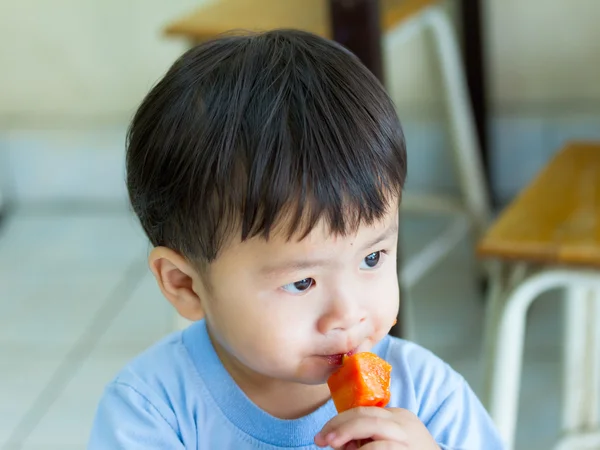 Portrait asian boy eating papaya on wood tip.