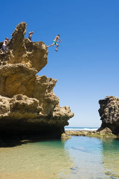 People jumping off a cliff into rock pool