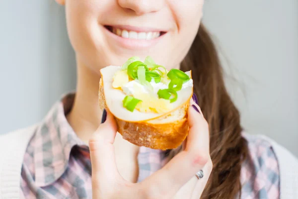 Woman eating sandwich with cheese and green vegetables onion