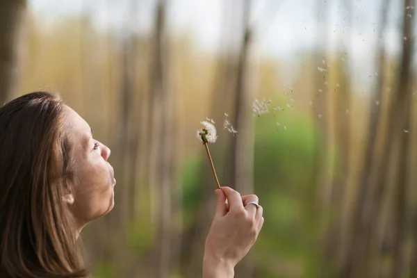 Young woman in the park holding blowing dandelion flower seed