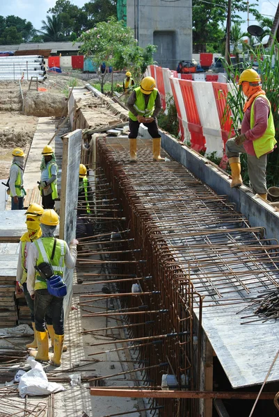 Construction workers fabricate retaining wall reinforcement bar and formwork at the construction site.