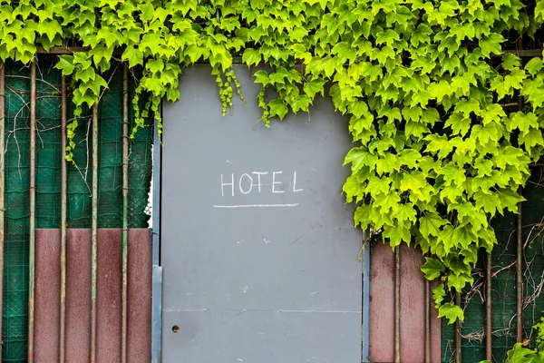 Hotel entrance door with sign in a fence with green foliage
