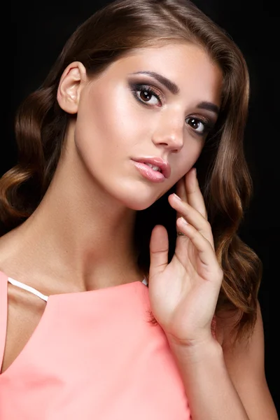 Beautiful woman in a pink romantic dress with smooth wavy hair and smoky eyes make up  on black background