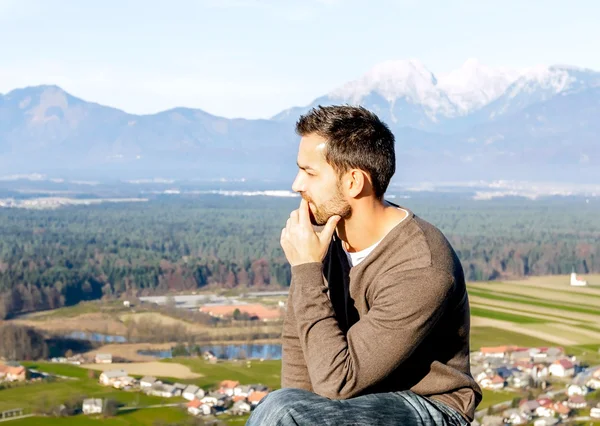 Handsome male tourist with deep thinking pose at top of mountain with misty beautiful European alps