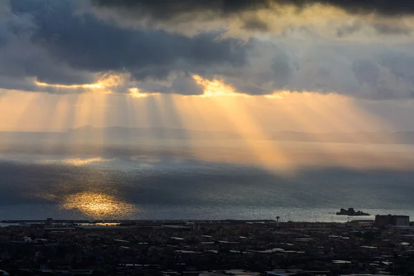 Sunbeams over the city. Sun cuts through the clouds over the sea