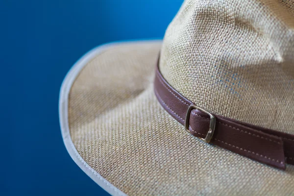 Blurred blue image of a cream hat with white fringe and brown strap
