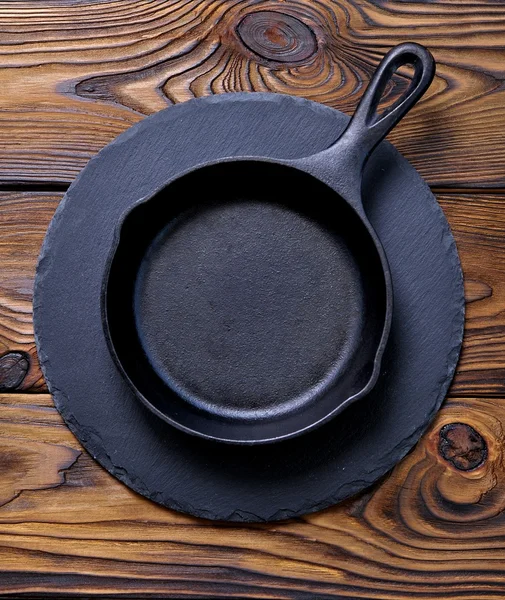 Iron frying pan on a serving board on wooden background.