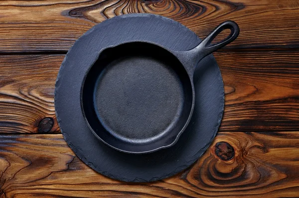 Iron frying pan on a serving board on wooden background.