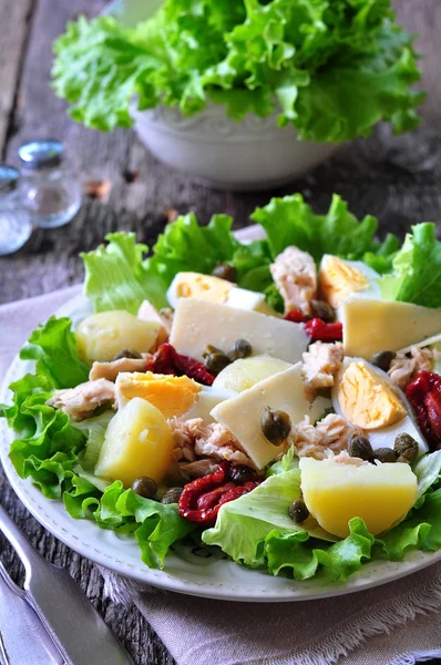 Salad of lettuce, iceberg lettuce, with canned tuna, dried tomatoes, boiled potatoes, capers and parmesan cheese, dressed with olive oil. Selective focus. rustic style.