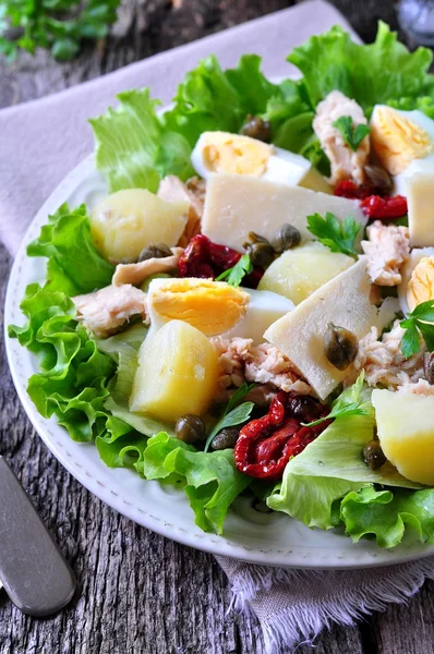 Salad of lettuce, iceberg lettuce, with canned tuna, dried tomatoes, boiled potatoes, capers and parmesan cheese, dressed with olive oil. Selective focus. rustic style.