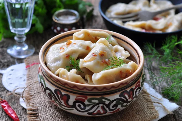 Dumplings with potatoes and mushrooms with fried onions in a traditional ceramic plate on a wooden table. Ukrainian traditional cuisine. rustic style. selective focus