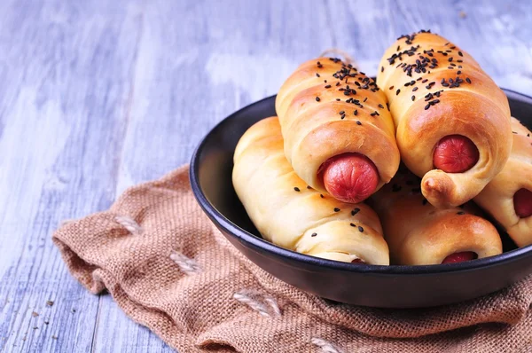 Sausage baked in pastry in a black plate on a light wooden background