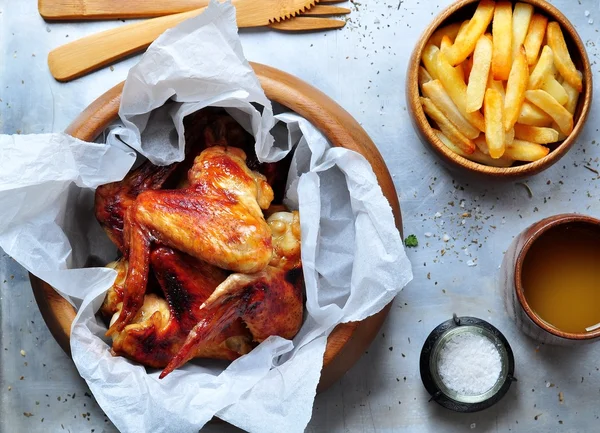 Grilled chicken wings with french fries in a wooden bowl on the aluminum background