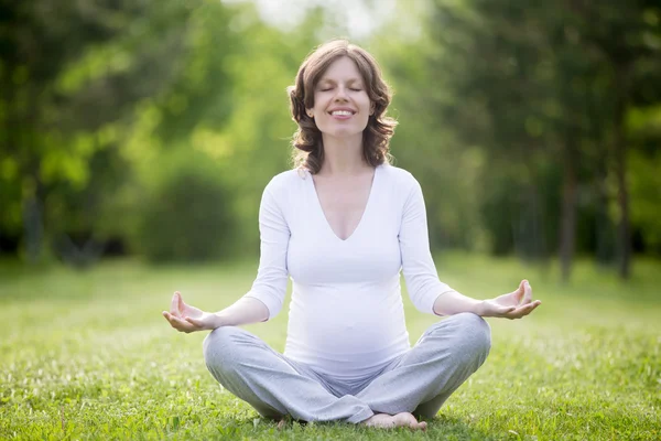 Happy pregnant woman meditating in park